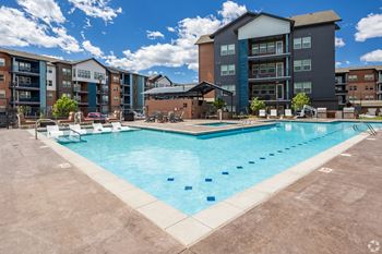 a swimming pool with lounge chairs and umbrellas in front of an apartment building